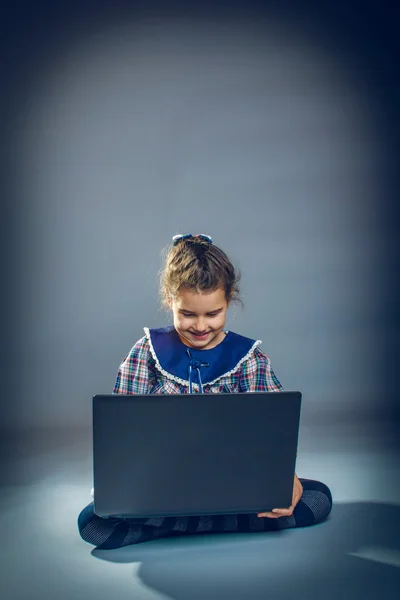 Adolescente chica jugando el suelo en portátil en un fondo gris —  Fotos de Stock
