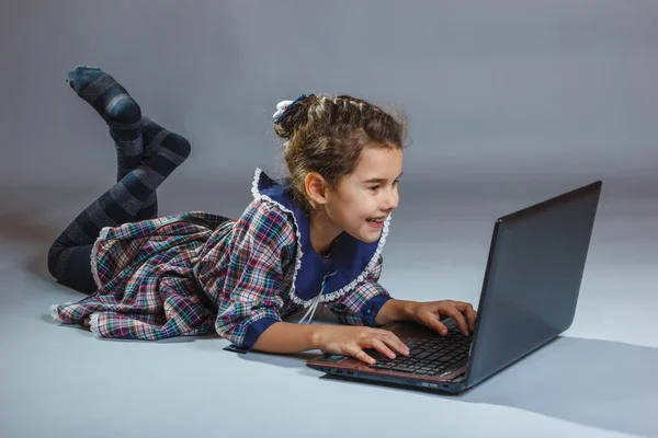 Bebê menina jogar laptop no fundo cinza — Fotografia de Stock