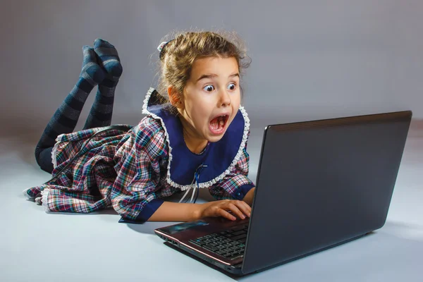 Baby Mädchen spielt Laptop überrascht auf grauem Hintergrund — Stockfoto