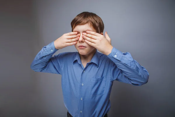 Adolescente chico cerrado ojos con sus manos en un gris fondo — Foto de Stock