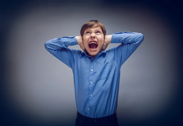 Teenager boy shouts shut  ears opened his mouth on gray bac — Stock Photo, Image