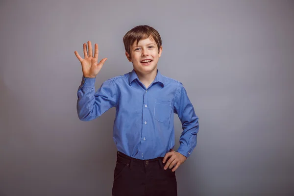 Adolescente ragazzo onde la sua mano su sfondo grigio — Foto Stock