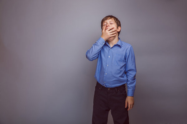 мальчик-подросток зевает на сером фоне
