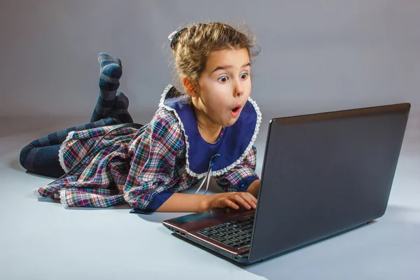 A criança menina está jogando em um laptop surpreso no backgr cinza — Fotografia de Stock