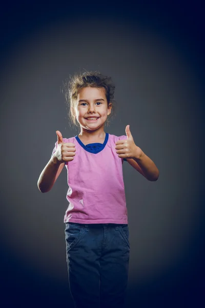 The girl child is showing thumbs up gesture yes on a gray backgr — Stock Photo, Image