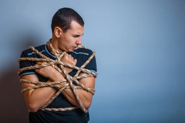 The man of European appearance brunet tied with rope on a gray b — Stock Photo, Image