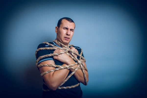 Mannetje van Europees uiterlijk brunet vastgebonden met touw op een grijze rug — Stockfoto