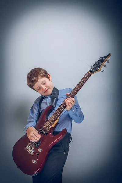 Teenie-Junge spielt Gitarre auf grauem Hintergrund Kreuzprozess — Stockfoto