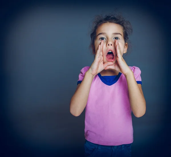 Teen ragazza ha aperto la bocca sta chiamando su uno sfondo grigio croce — Foto Stock