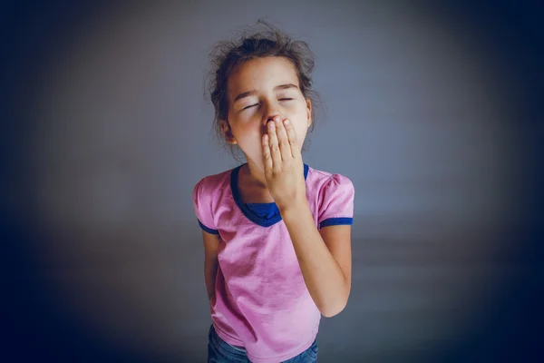 The girl child is tired closes her mouth yawns on a gray backgro — Stock Photo, Image