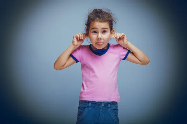 Child girl showing tongue pulls ears on gray background cross pr — Stock Photo, Image