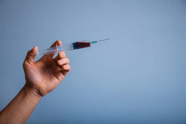 Hand holding syringe with drug addict on a gray background — Stock Photo, Image