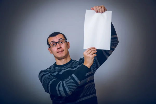 European-looking male holding a white sheet of paper on gray — Stock Photo, Image