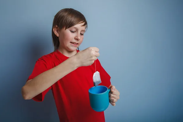 Boy teenager European appearance in a red shirt puts a tea bag i — Stock Photo, Image