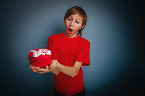 Niño de aspecto europeo de diez años sosteniendo una caja de regalo en una b gris —  Fotos de Stock
