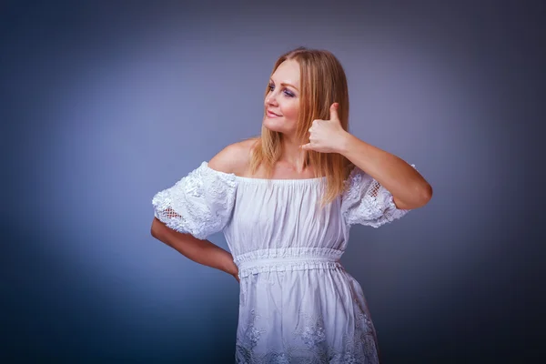 Chica rubia europea apariencia en un vestido blanco muestra un signo de —  Fotos de Stock