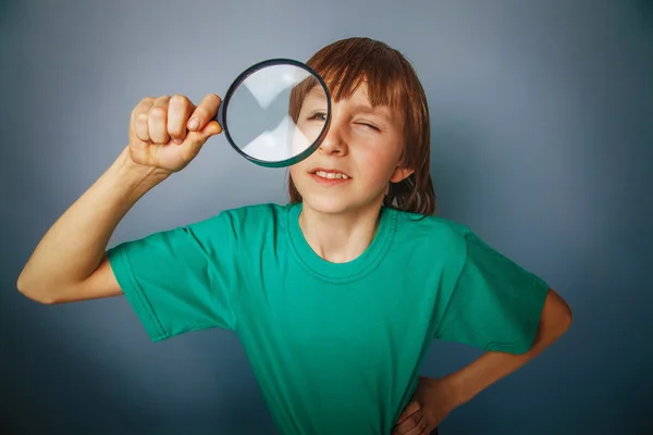European-looking boy of ten years a joke, looking through a magn — Stock Photo, Image