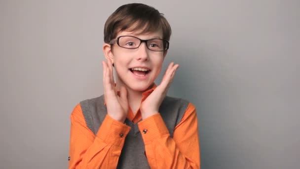 Menino adolescente surpresa felicidade alegria ondas suas mãos por dez anos óculos no fundo cinza slow-motion vídeo — Vídeo de Stock
