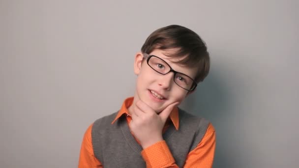 dospívající chlapec úsměvem zkušenosti štěstí drží ruku na bradě v brýlích na šedém pozadí desetiletí