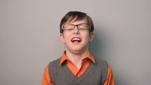 Genç çocuk komik gülüyor gözlüklü başını geri gri bir arka plan üzerinde on yıl attı — Stok video
