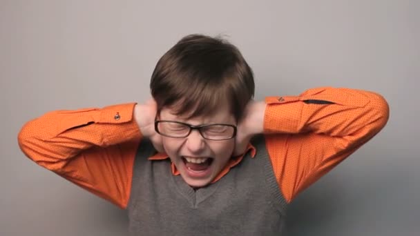 Teenager boy closed his ears with his hands loud sound in glasses on gray background — Stock Video