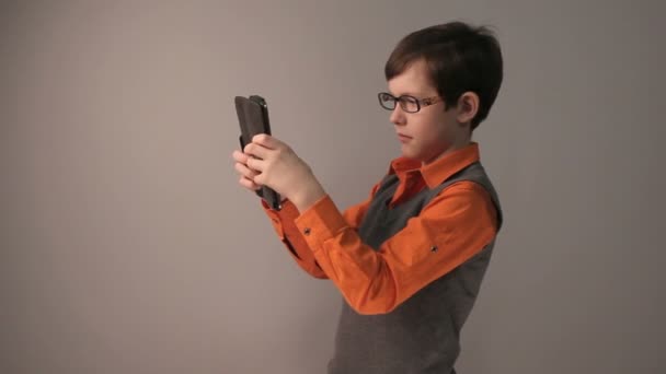 Fiú tinédzser játszik tabletta szívesen meglepett a szemüveg szürke háttér — Stock videók