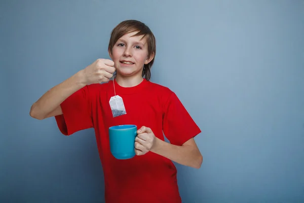 Boy, teenager, twelve years in the red shirt drinks tea bag — Stock Photo, Image