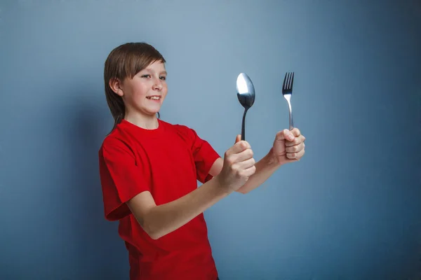 Jugendlicher Junge im roten Hemd zwölf Jahre mit Löffel und Gabel, — Stockfoto