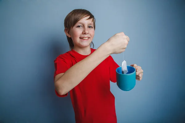 Teenager boy twelve years in a red shirt holding a cup of tea, a — Stock Photo, Image