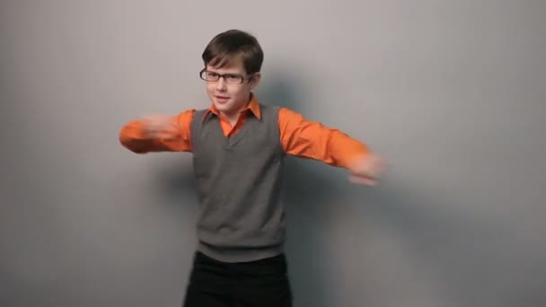 Мальчик-подросток танцует смешно размахивая руками в очках десять лет на сером фоне — стоковое видео