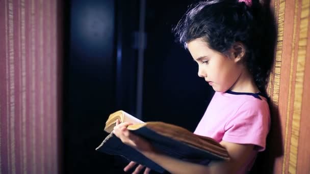 Adolescente niña leyendo un libro mientras está de pie contra una pared en el apartamento volteando página — Vídeos de Stock