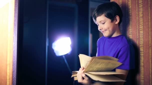 Teenager boy child reads book, standing against the wall in apartment page flipping — Stock Video