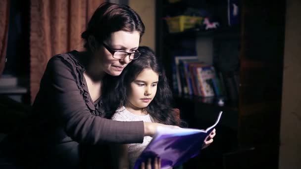 妈妈带眼镜的女人和她的女儿做作业的年轻女孩读本书决定叶 — 图库视频影像