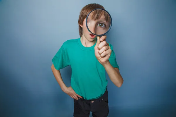 European-looking boy of ten years a joke, looking through a magn — Stock Photo, Image