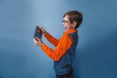 Tablet elinde tutan bardaklarda on yıllık Avrupa görünümlü oğlan mavi bir arka plan üzerinde çalış