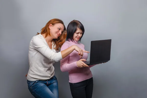 Tre flickor europeiskt utseende flickvän tittar på en dataskärm på en grå bakgrund, överraskning känslor — Stockfoto