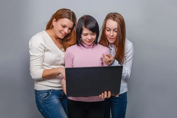 Tre flickor europeiskt utseende flickvän titta på datorskärmen på en grå bakgrund, överraskning känslor — Stockfoto