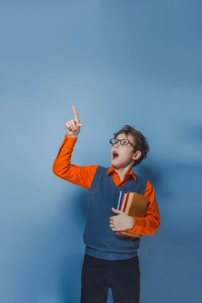 Niño de aspecto europeo de diez años en gafas pulgares hacia arriba, la idea del libro sobre un fondo gris —  Fotos de Stock