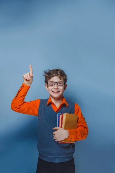 Niño de aspecto europeo de diez años en gafas pulgares hacia arriba, la idea del libro sobre un fondo azul —  Fotos de Stock