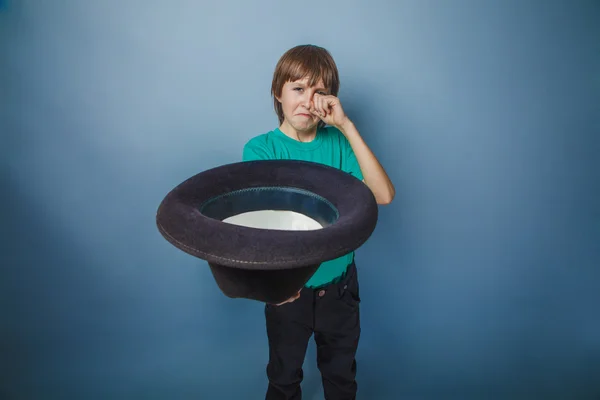 Європейський дивлячись хлопчик десяти років жебрак холдингу капелюхом у руці на синьому фоні — стокове фото