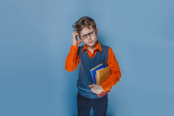 Europäisch aussehender Junge von zehn Jahren mit Brille denkt intensiv Buch auf blauem Hintergrund — Stockfoto