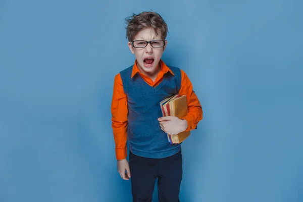 Ragazzo europeo di dieci anni in occhiali ha aperto la bocca gridando tenendo un libro su uno sfondo blu — Foto Stock