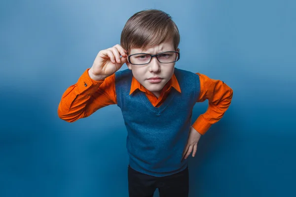 Niño de aspecto europeo de diez años en gafas frunciendo el ceño, infeliz sobre un fondo azul — Foto de Stock