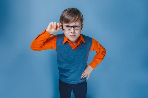 Niño de aspecto europeo de diez años en gafas frunciendo el ceño, infeliz sobre un fondo azul — Foto de Stock