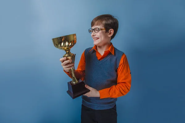 Menino de aparência europeia de dez anos em óculos segurando um prêmio copo em um fundo azul — Fotografia de Stock
