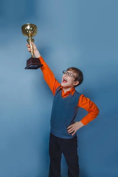 Europese uitziende jongen van tien jaar in glazen holding een kop award op een blauwe achtergrond — Stockfoto