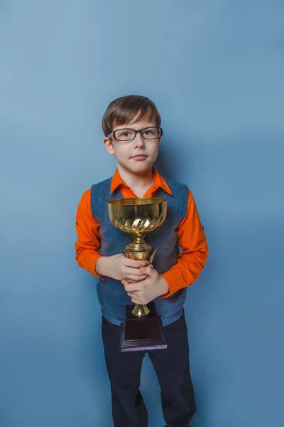 Menino de aparência europeia de dez anos em óculos segurando uma xícara, alegria prêmio em um fundo azul — Fotografia de Stock