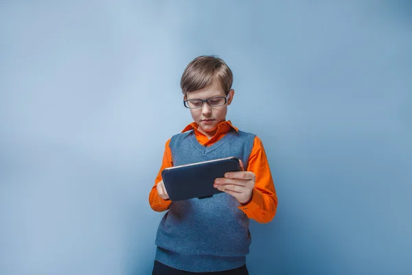 Europäisch aussehender zehnjähriger Junge in Brille mit Tablet in der Hand auf blauem Hintergrund — Stockfoto