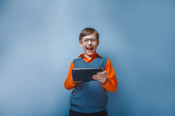 Europäisch aussehender zehnjähriger Junge in Brille mit Tablet in der Hand auf blauem Hintergrund — Stockfoto