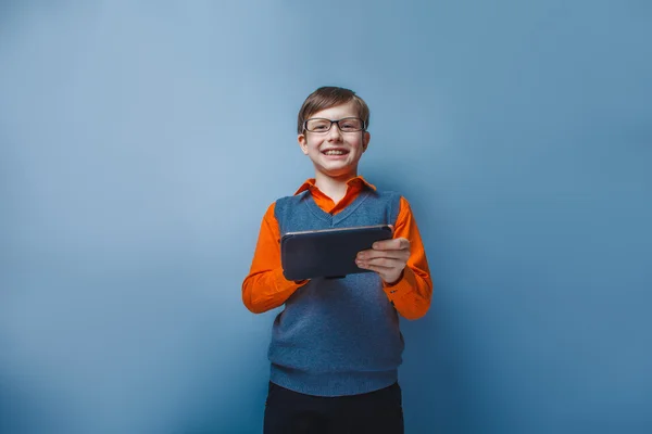 Chico de aspecto europeo de diez años en gafas sosteniendo la tableta en la mano sobre fondo azul —  Fotos de Stock